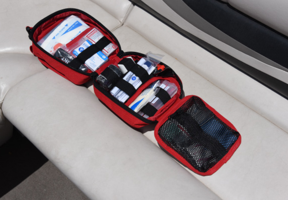 An open red first aid kit lying on a boat seat, fully stocked with bandages, gauze, and medical supplies.