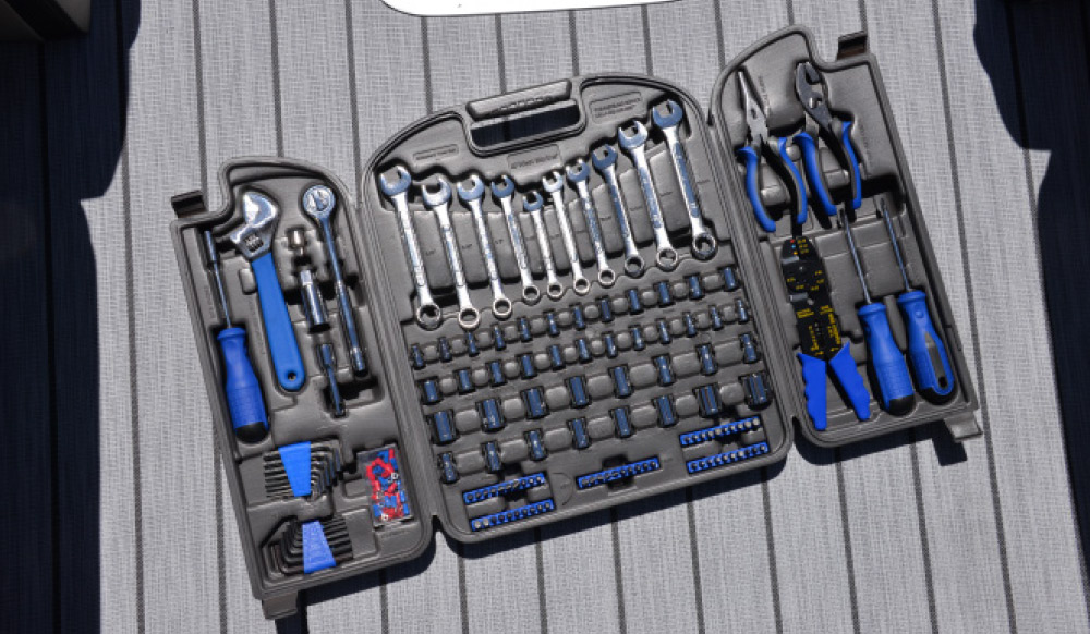 A complete marine tool kit in a grey plastic case, containing wrenches, sockets, and pliers, spread open on a boat deck.