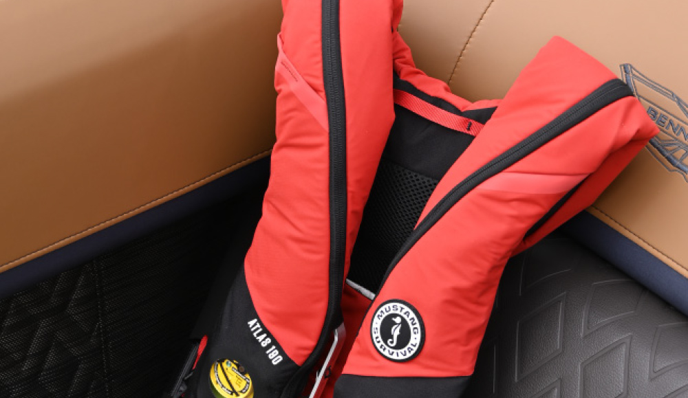 A red Mustang Survival Atlas 190 inflatable life jacket resting on a tan boat cushion.