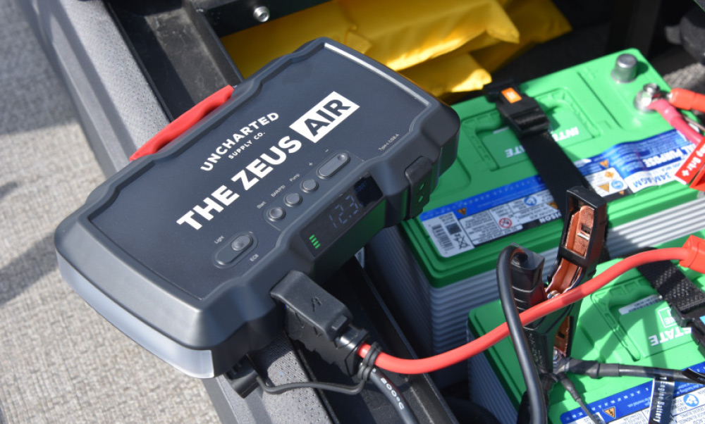 A Zeus Air portable jump starter and air compressor by Uncharted Supply Co. connected to a green boat battery.
