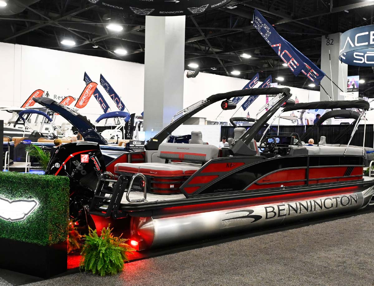 Red and black Bennington pontoon boat featuring a large Mercury outboard motor and a black sports tower on an indoor showroom floor.