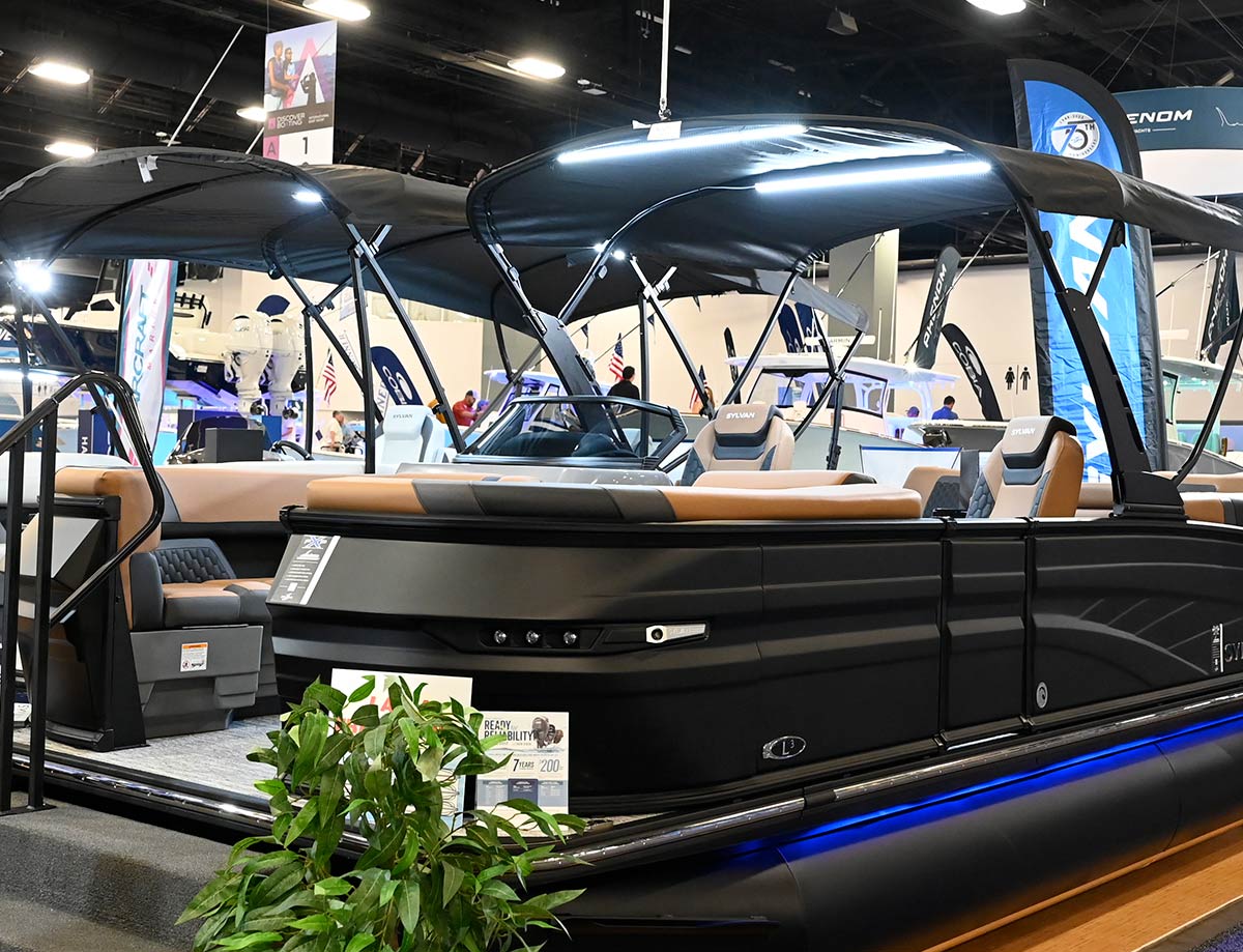 A black Sylvan pontoon boat with tan and black seats and an overhead canopy with integrated LED lighting.
