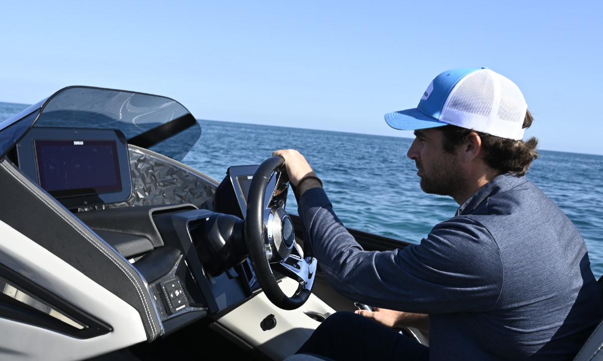 A man in a blue cap steers a boat at the 2026 Miami Boat Show, using a Barletta wheel and Simrad digital display.