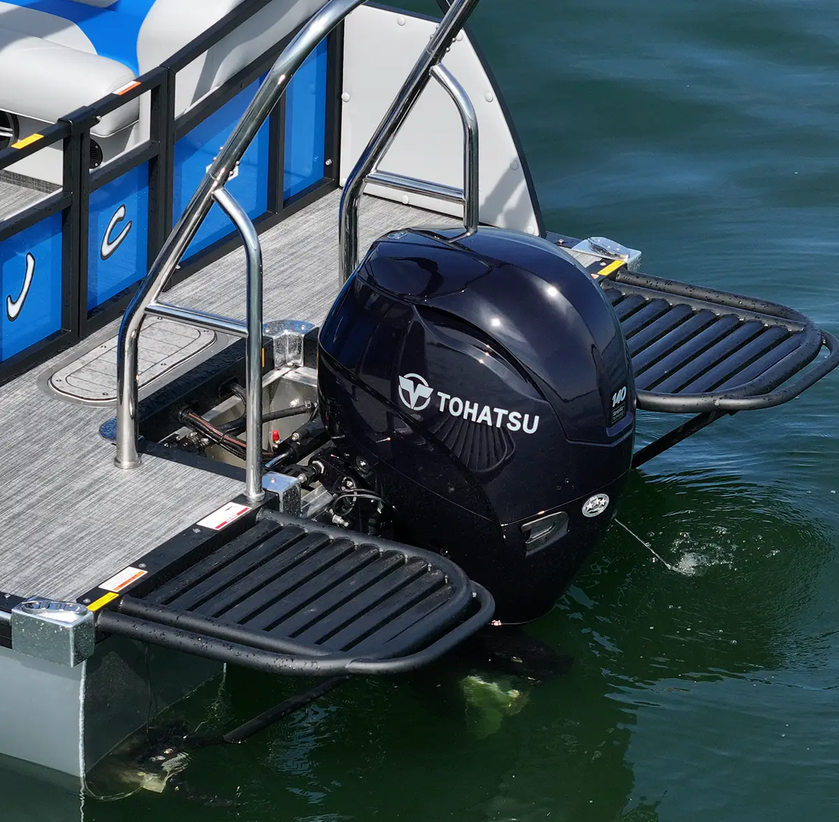 The rear deck of a JC Spirit pontoon boat, featuring a black Tohatsu 140 outboard motor flanked by two black textured swim platforms and stainless steel railings
