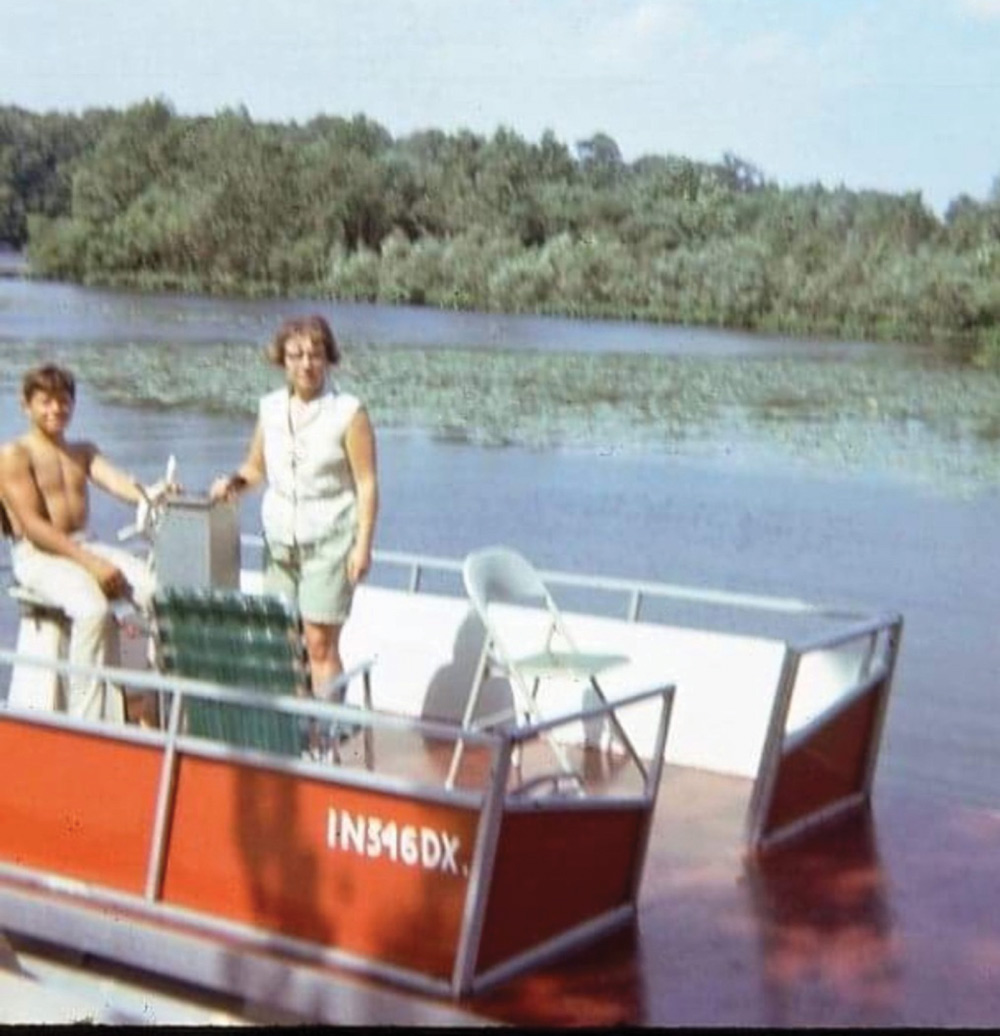 A vintage, grainy photo shows a man and woman on a small red and white pontoon boat on a river with dense green trees.