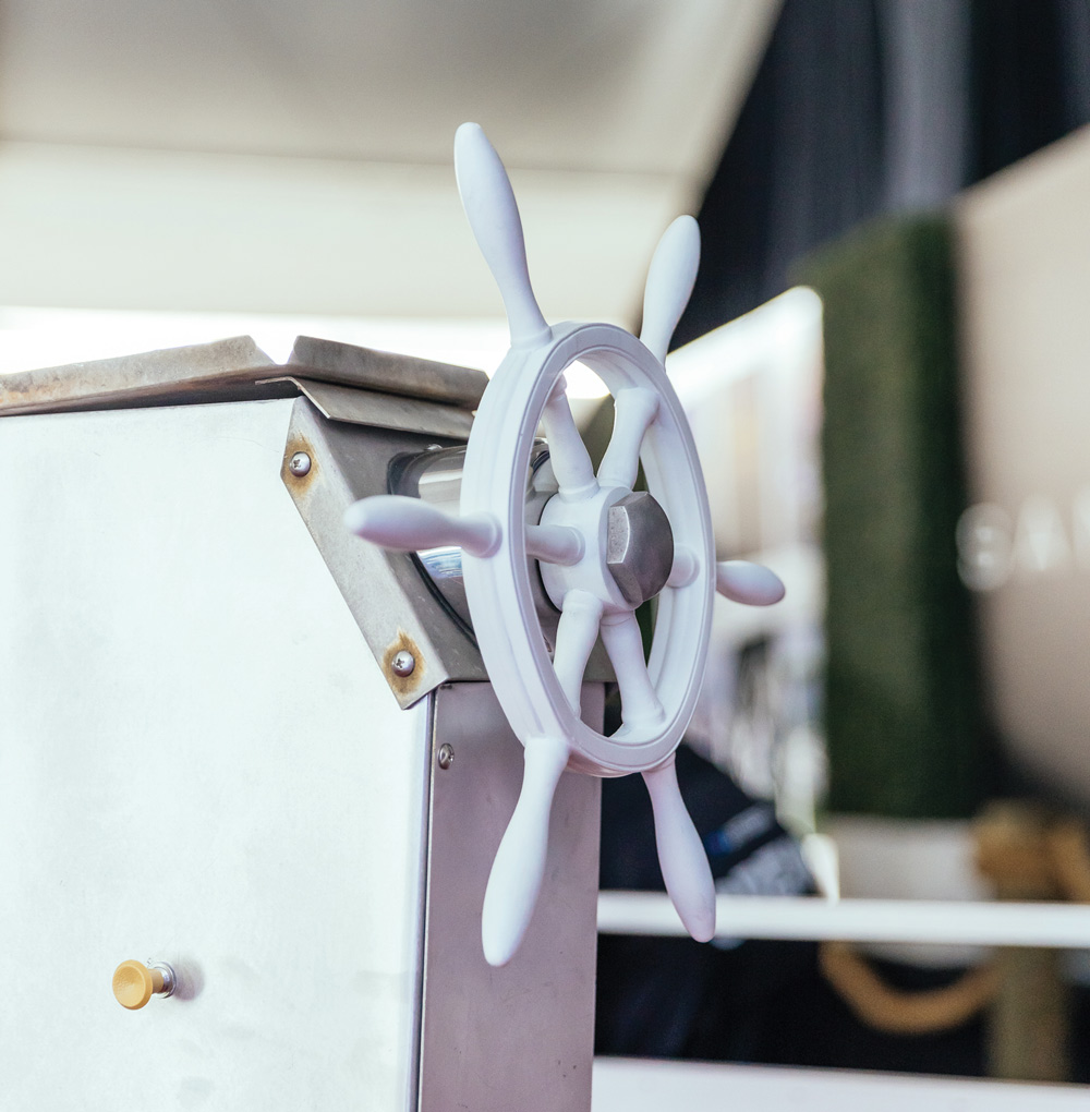 Close-up of a vintage-style white nautical steering wheel mounted on a silver control pedestal.