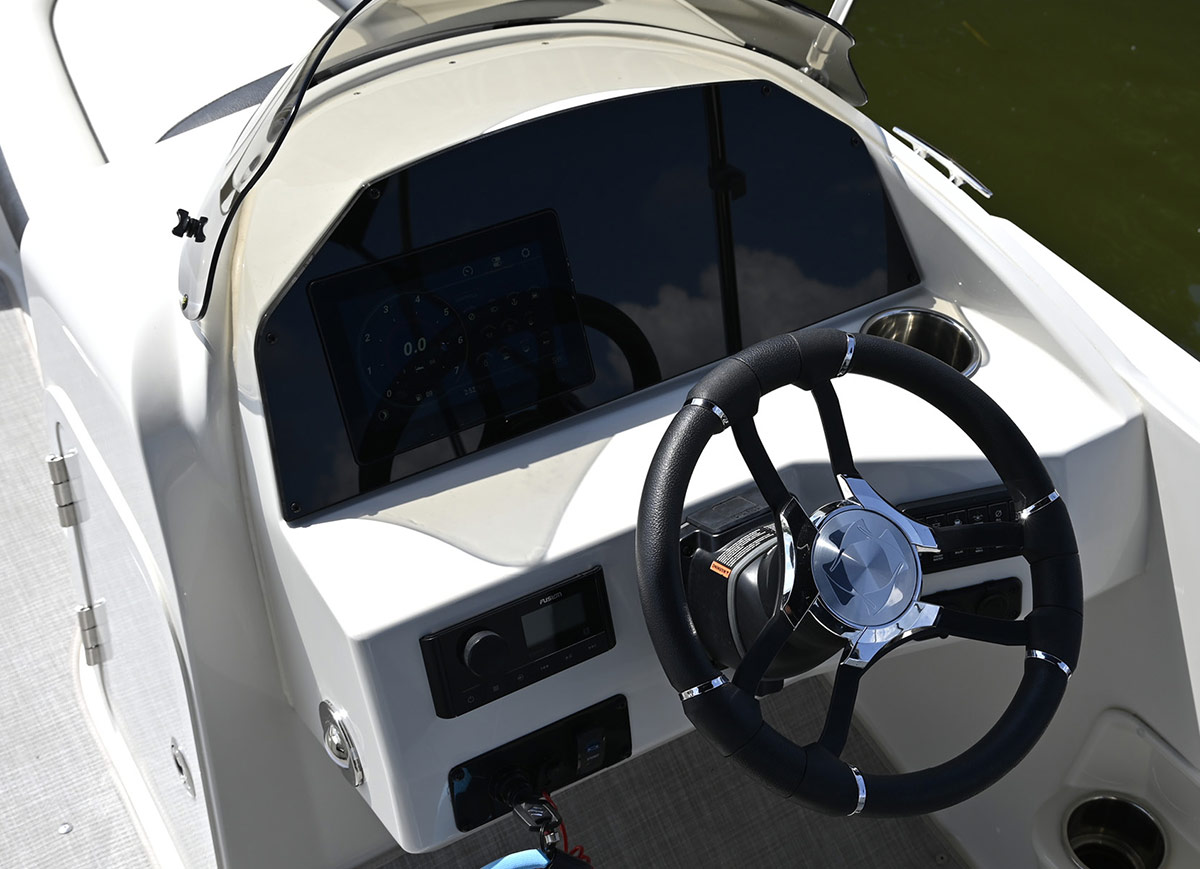 Close-up of a white boat's helm featuring a black and silver steering wheel, a digital dashboard display screen, and a radio control unit.