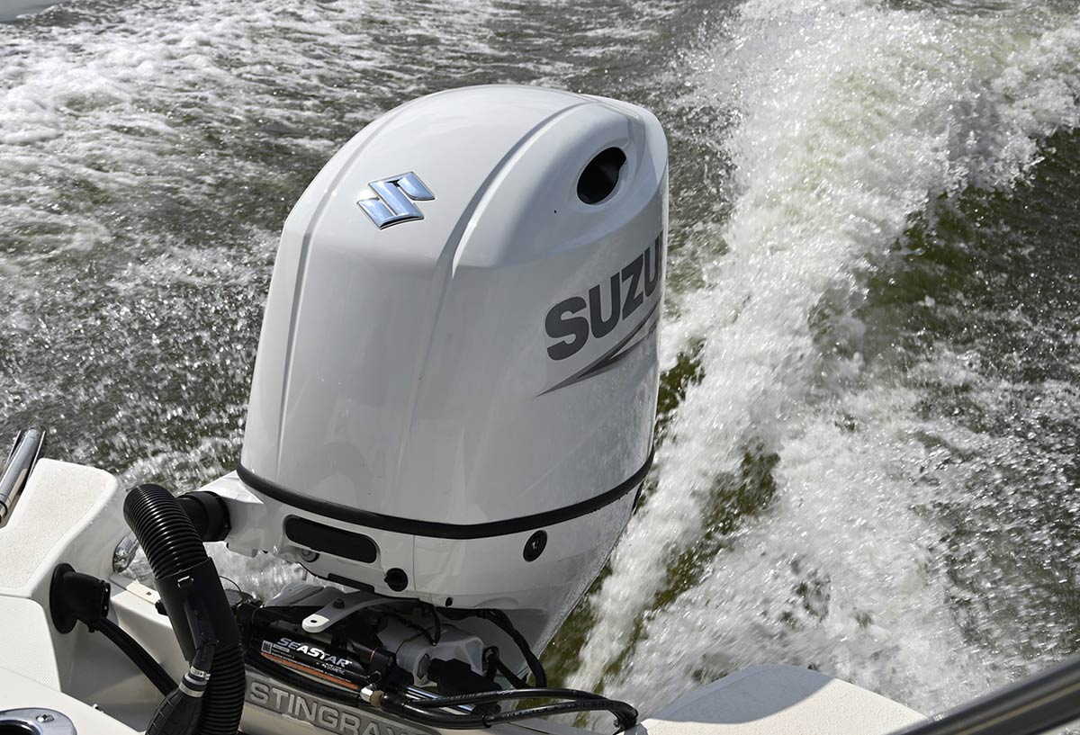 A white Suzuki outboard motor on the back of a Stingray boat, creating a large, splashing white wake as it moves through the water.
