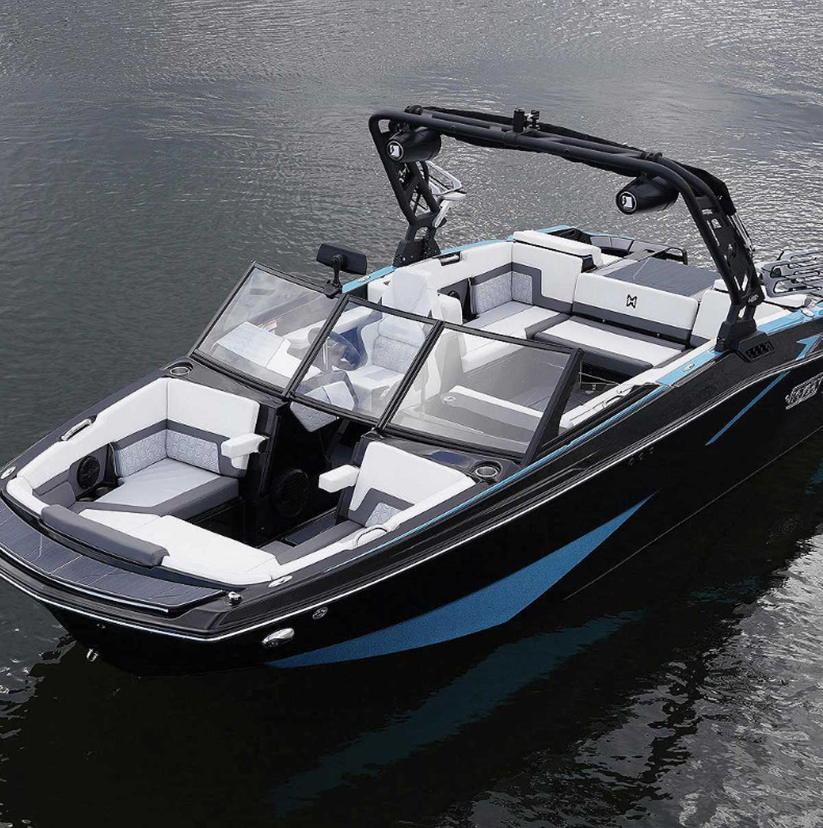 Sleek black and blue wakeboard boat on calm water, featuring a prominent black wake tower with speakers and spacious white and grey interior seating.