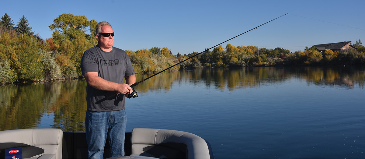 A man in sunglasses fishes from a boat on a calm lake