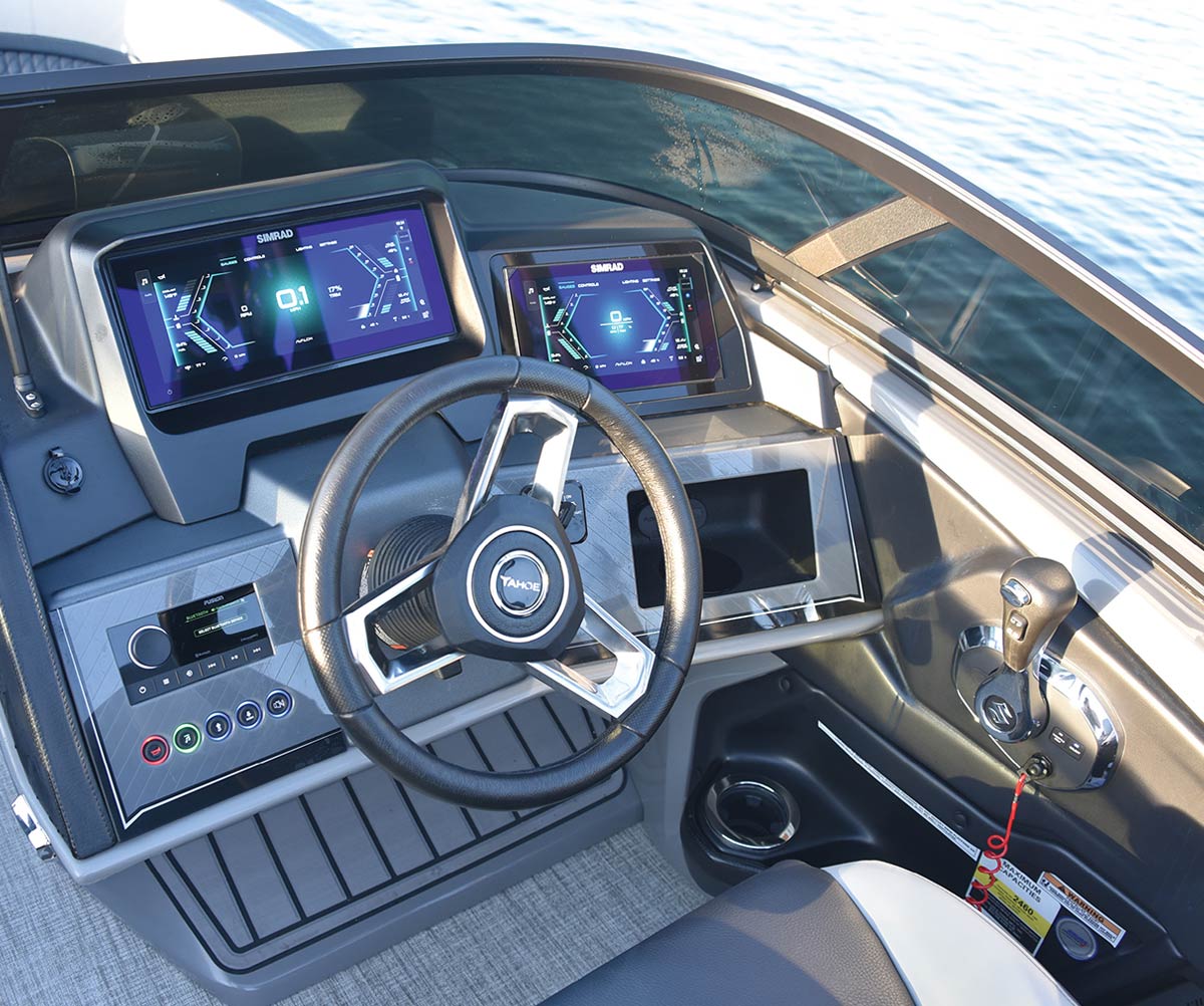Close-up of a modern Tahoe boat helm featuring dual Simrad digital displays, a Fusion marine stereo, and Suzuki throttle controls next to a black steering wheel with a "TAHOE" logo.