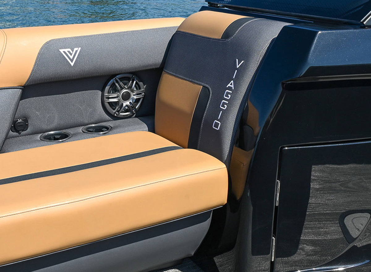 Two-tone tan and grey upholstered seating in a Viaggio boat, featuring the brand name on the backrest, a built-in speaker, and integrated cup holders next to a glossy black console.