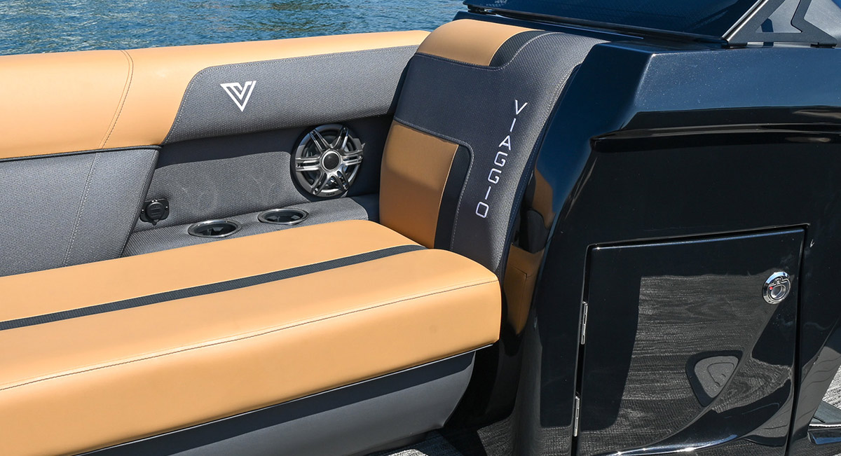 Two-tone tan and grey upholstered seating in a Viaggio boat, featuring the brand name on the backrest, a built-in speaker, and integrated cup holders next to a glossy black console.