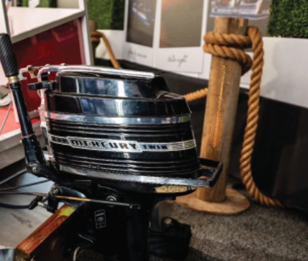 Black Mercury Twin outboard motor mounted on the transom of a small boat with a small wooden paddle leaning layered against a wooden piling wrapped in thick rope