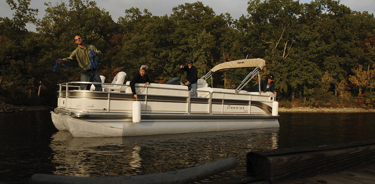 A group of people on a pontoon boat prepare to dock on a calm lake.