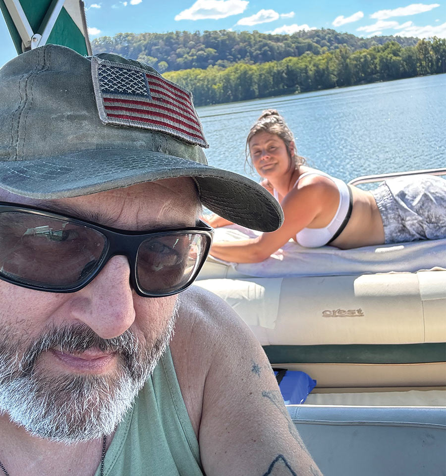 Close-up selfie of a man on a boat with a woman relaxing behind him.