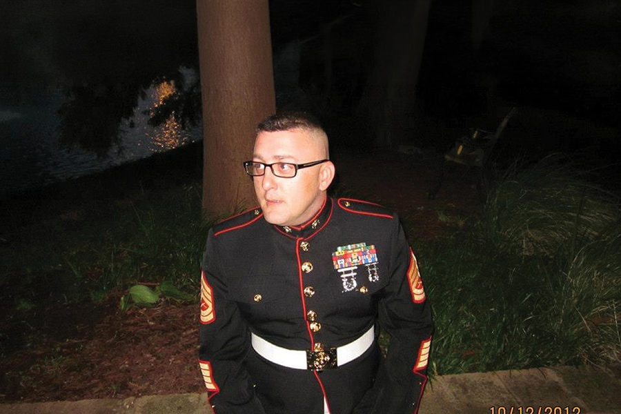 A man wearing glasses poses in a formal military dress uniform with medals outdoors.