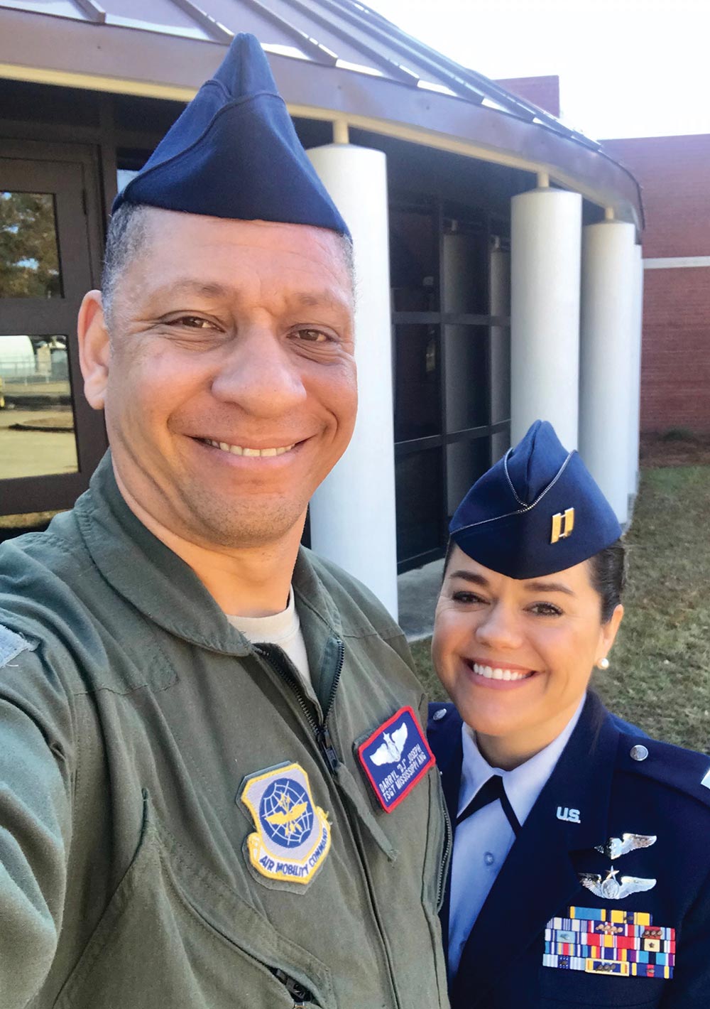 A smiling man and woman pose close together indoors wearing U.S. Air Force uniforms.
