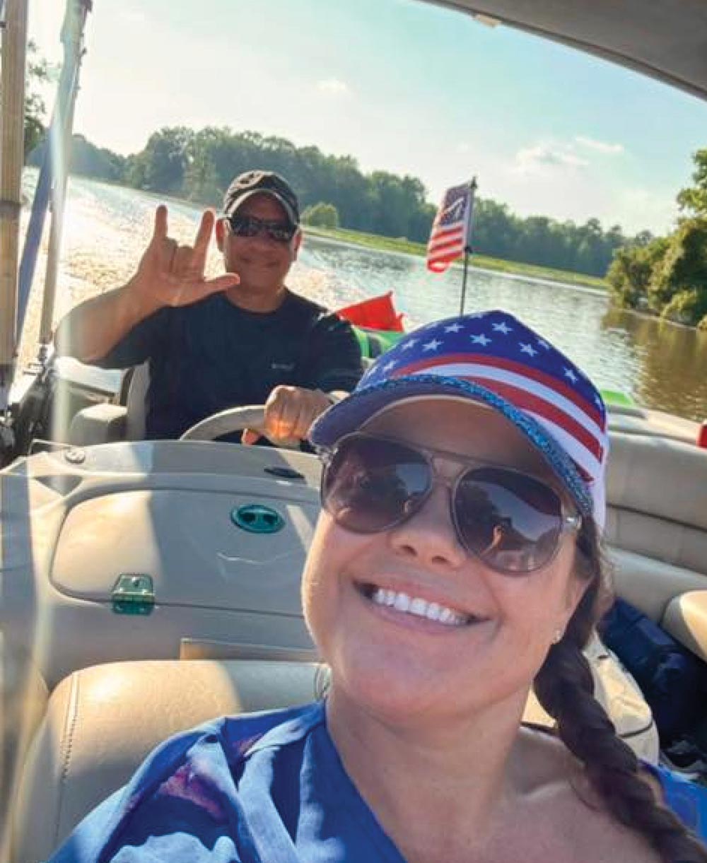 A close-up selfie of a smiling couple riding in a boat on a sunny river.
