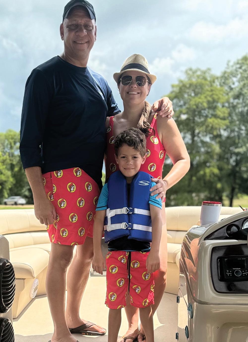 A man, woman, and child wear matching red Buc-ee's swimwear on a pontoon boat.