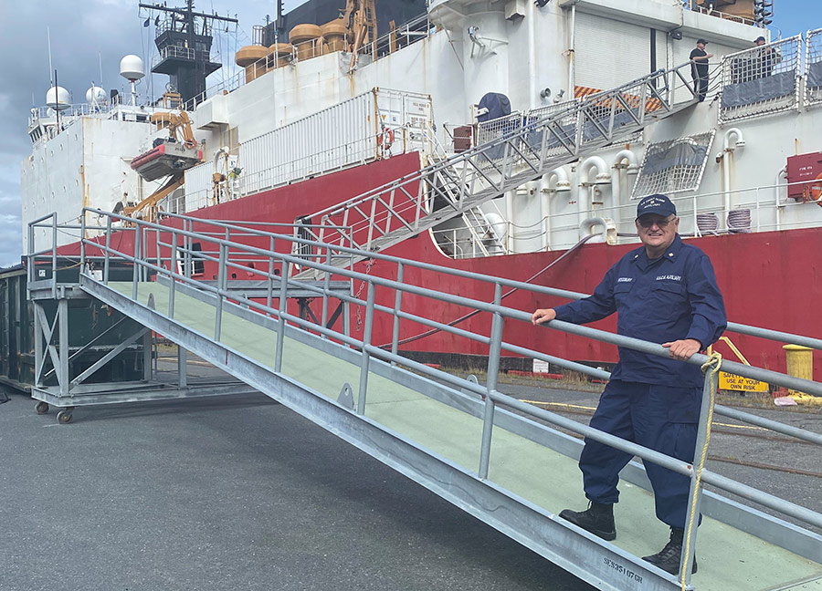 A man in uniform stands on a metal ramp leading up to a large ship.