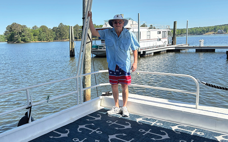A man wearing a sun hat and shorts stands on a boat on a lake.