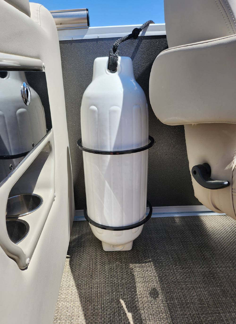 A large white boat fender secured vertically in a black ring holder inside a pontoon boat's interior.