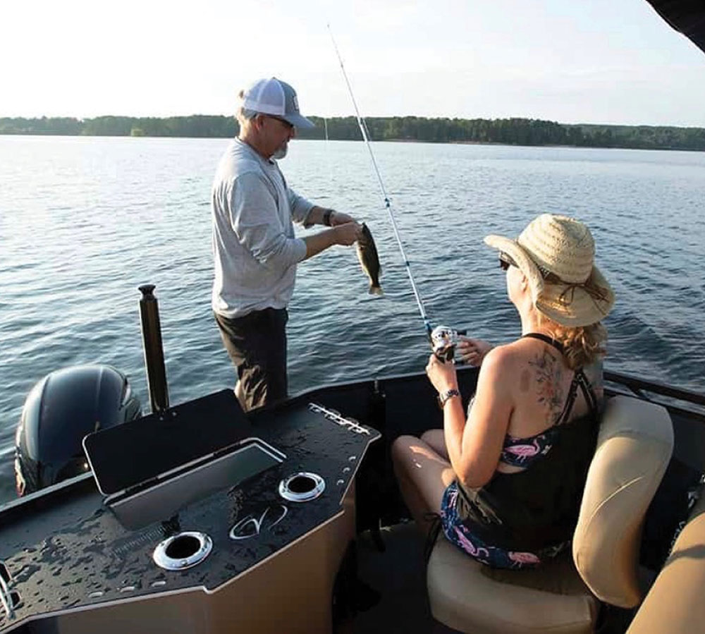 A man and woman fishing together from the stern of a pontoon boat.