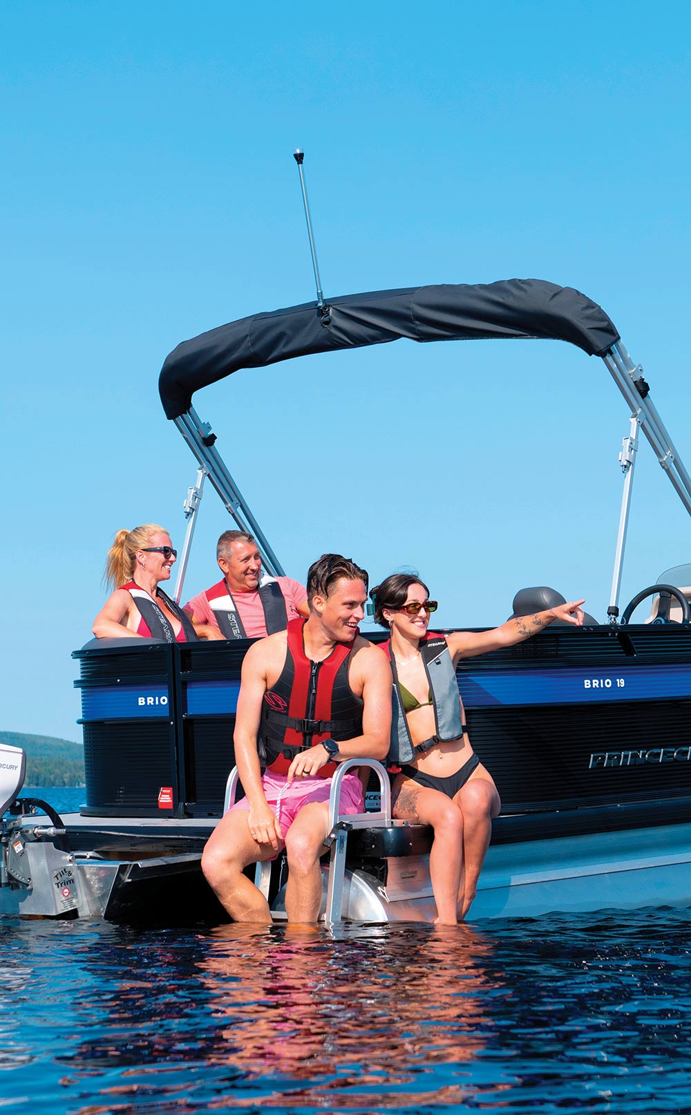 Four people smile while sitting on the back of a pontoon boat.