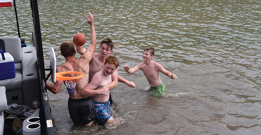 Four boys play a game of water basketball next to a boat.