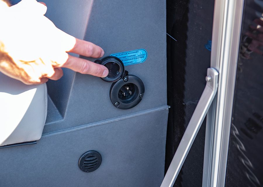 A hand opens a black protective cap on an AC plug for an accessory battery charger.