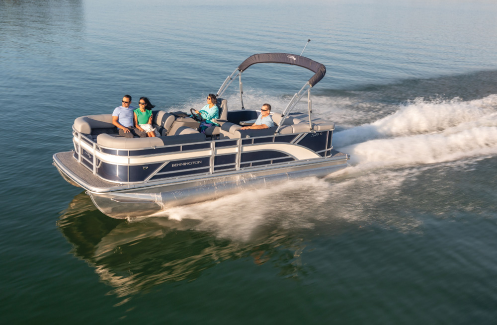 A blue Bennington pontoon boat with four passengers cruising on open water on a sunny day.