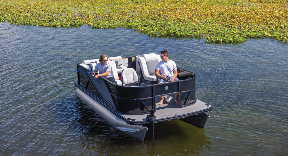 Two men fishing from a compact Godfrey Mighty G pontoon boat near lily pads on a lake.