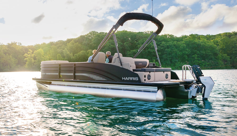 A Harris pontoon boat with a Mercury electric outboard motor anchored on calm water at sunset.