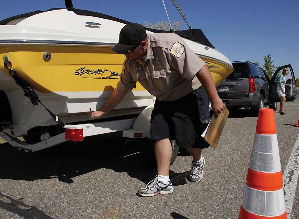 A park ranger inspecting the back of a yellow boat on a trailer.