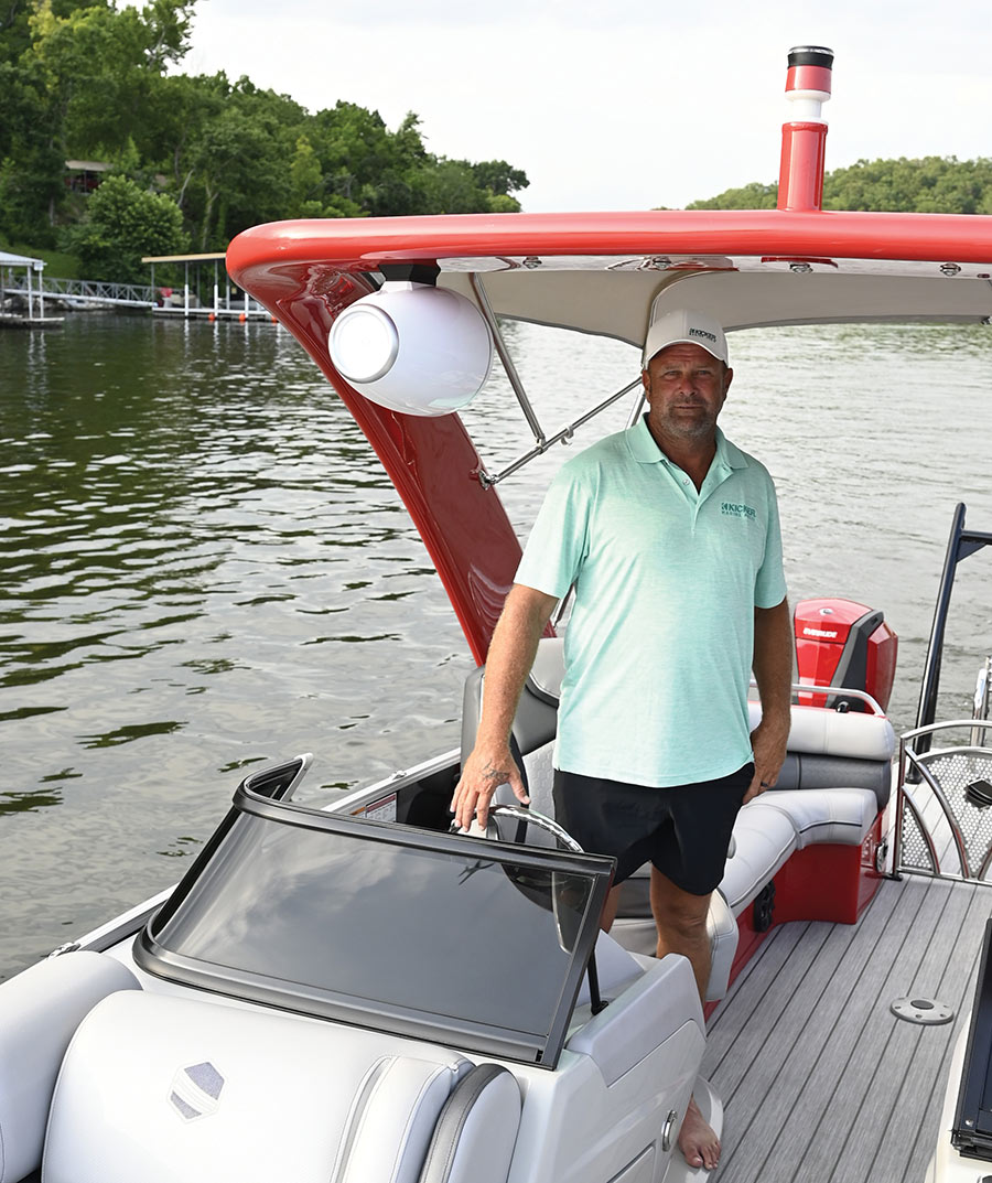 A man in a polo shirt stands at the helm of a red pontoon boat.
