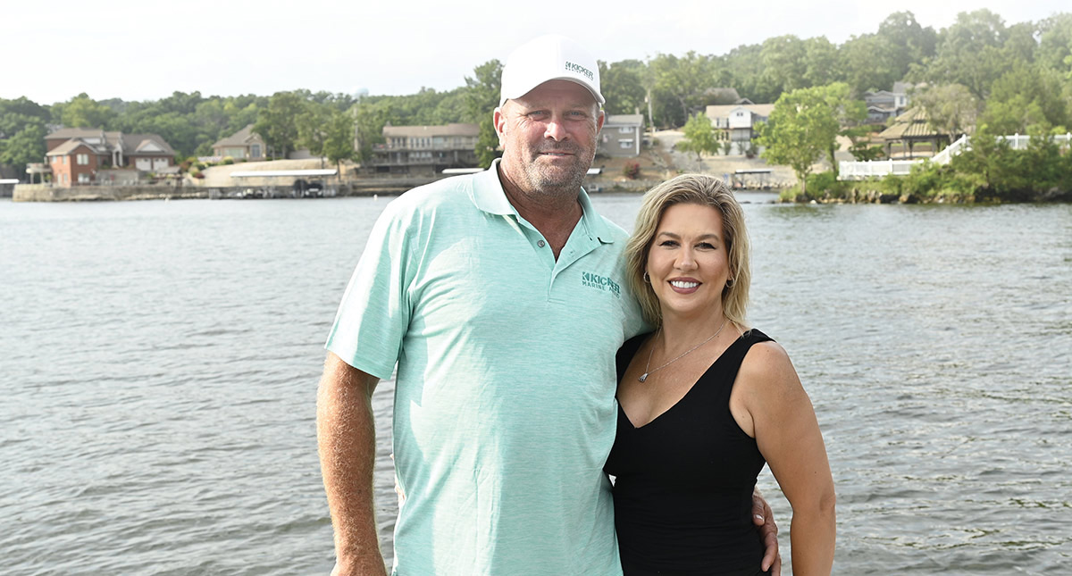 A smiling man and woman pose together on a boat with water behind them.