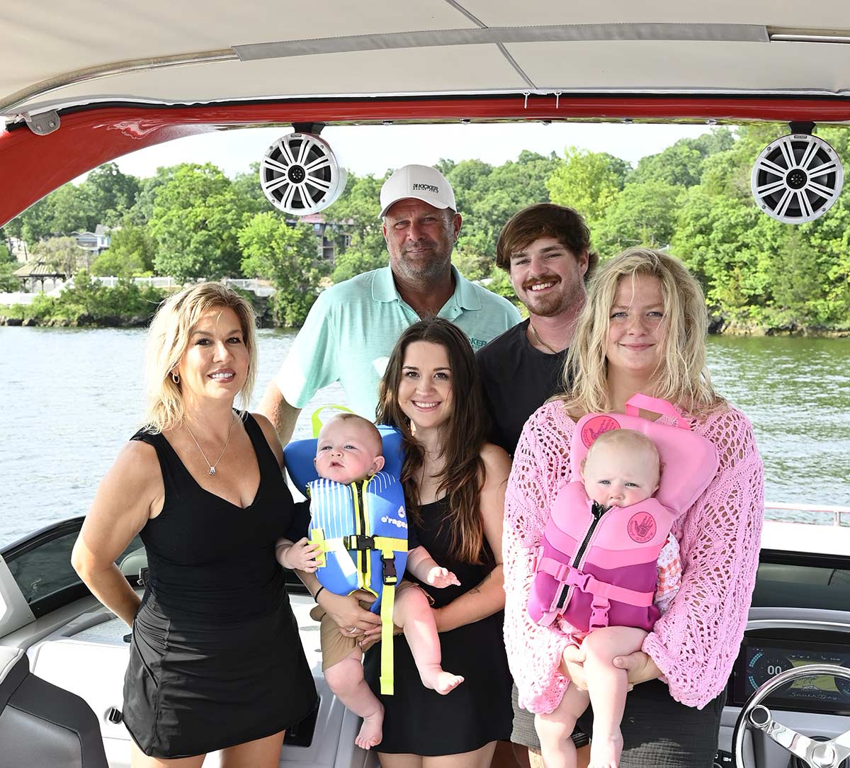 A family, including two babies in life vests, poses together on a pontoon boat.