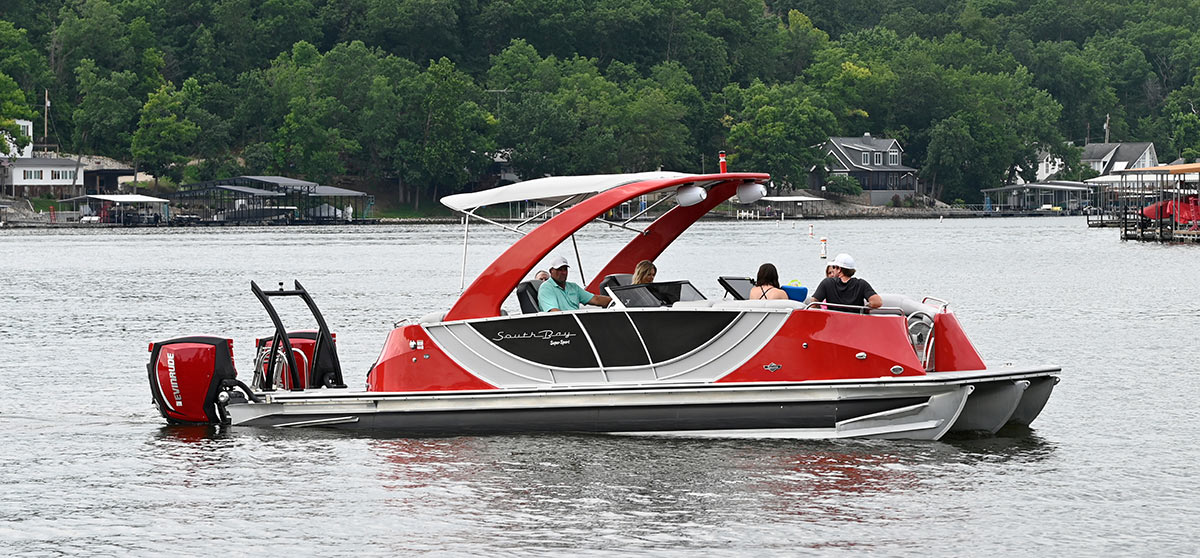 Side profile of a red South Bay pontoon boat cruising on calm lake water.