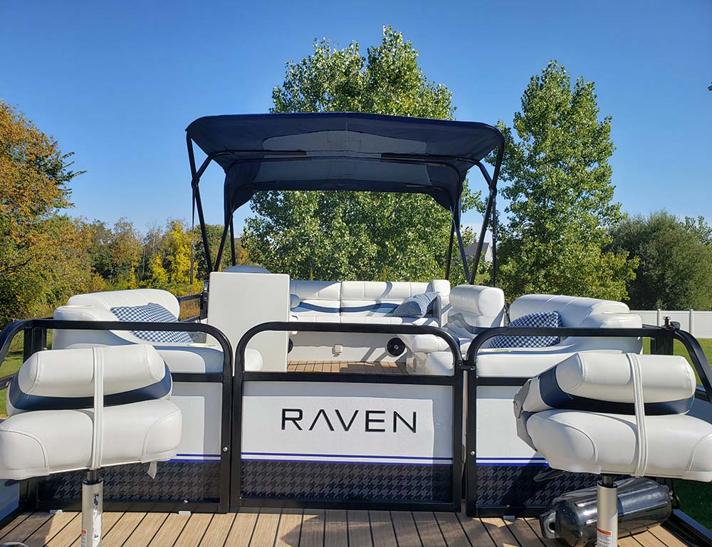 Rear-facing view of a white and navy Raven pontoon boat featuring swivel seats and plush seating.