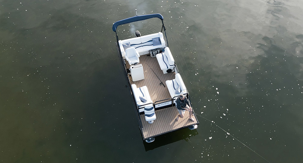 Aerial view of a Raven pontoon boat on open water with a man fishing from the bow.