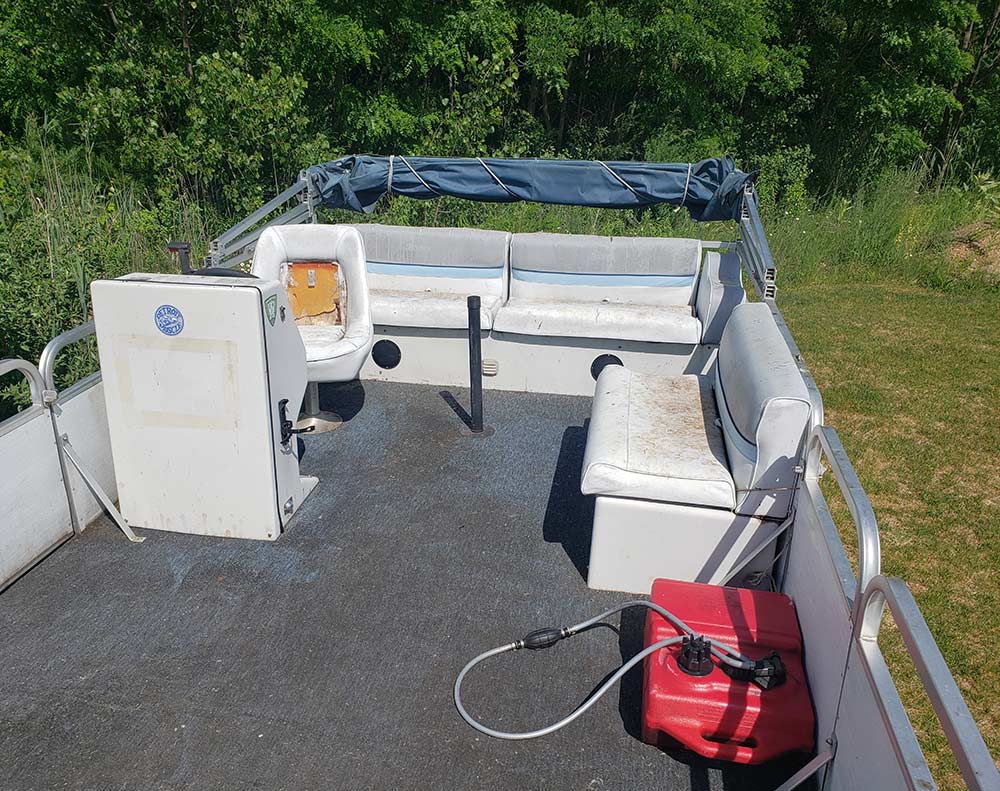 An overhead interior view of an older pontoon boat showing worn seating and carpet floor.