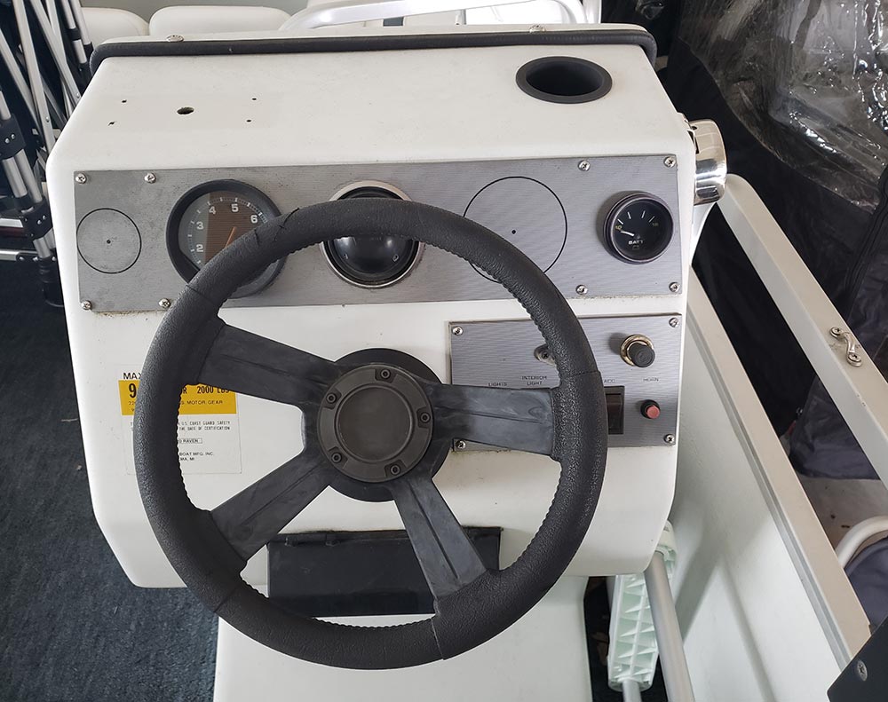 A close-up view of an older pontoon boat's white steering console and dashboard instruments.