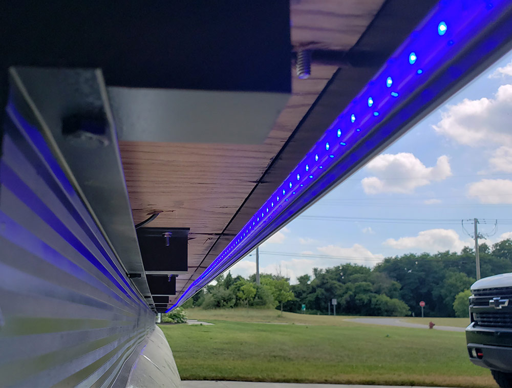 Close-up under the edge of a pontoon boat deck showing installed blue LED strip lighting.