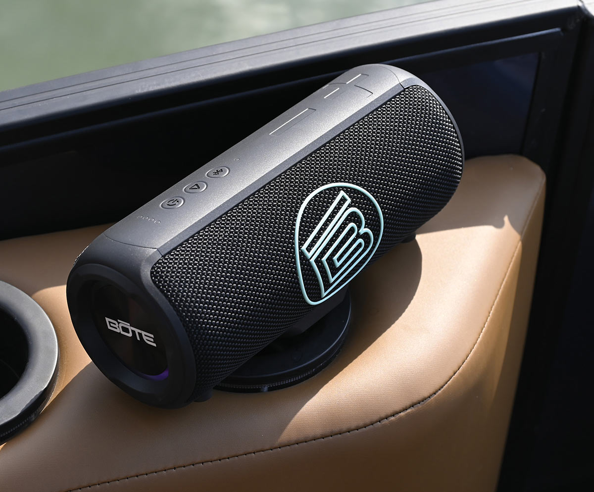 Close-up of a black BŌTE portable speaker with a light blue logo magnetically mounted on a tan leather boat seat armrest.