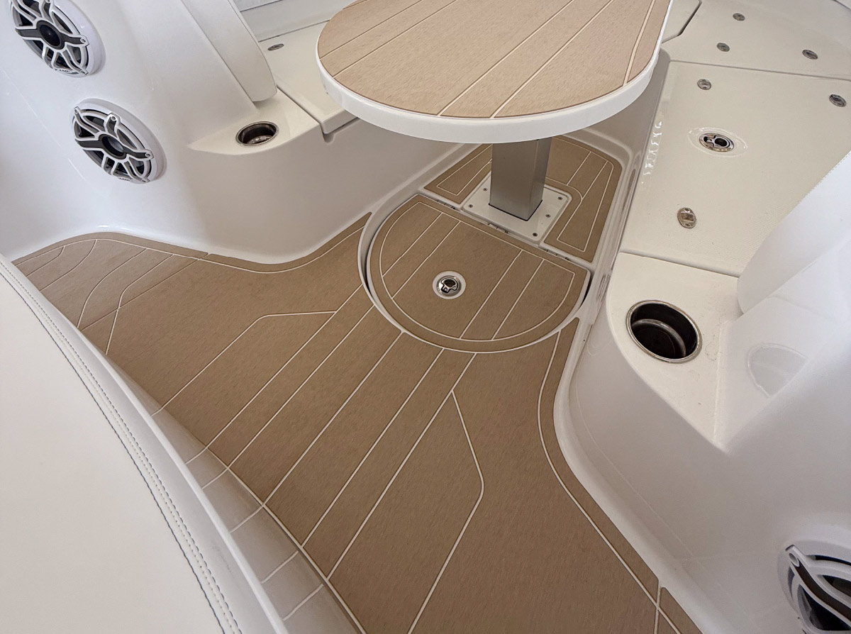 Boat interior showing custom faux-teak tan decking installed around a pedestal table and cup holders.