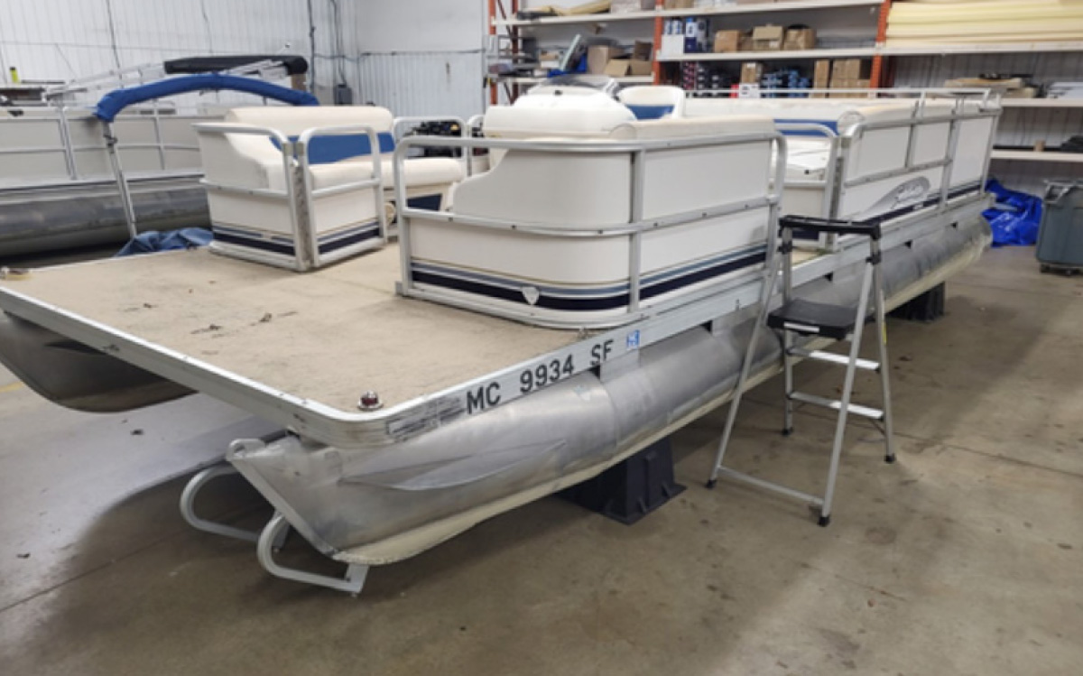 An older pontoon boat with worn flooring sitting indoors on support blocks during a renovation project.