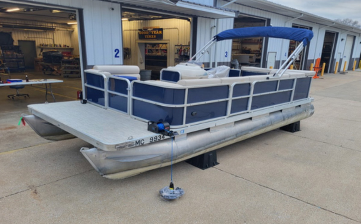 Restored blue pontoon boat with fresh grey decking, blue bimini top, and a bow anchor winch setup.