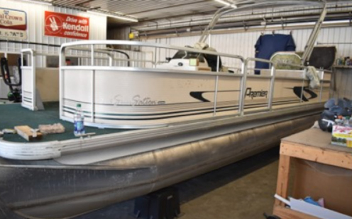 Premier SunSation pontoon boat with faded tan side panels parked inside a garage workshop.