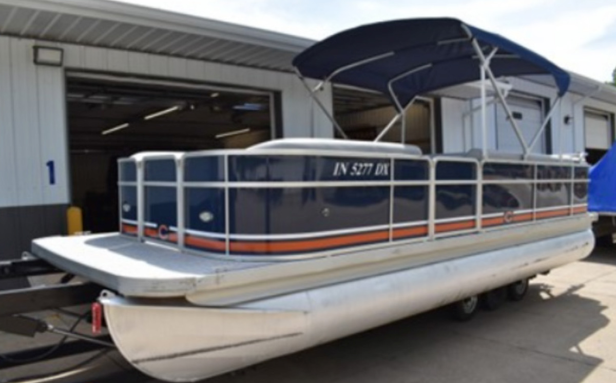Renovated navy blue pontoon boat with orange striping and a bimini top parked outside a service bay.